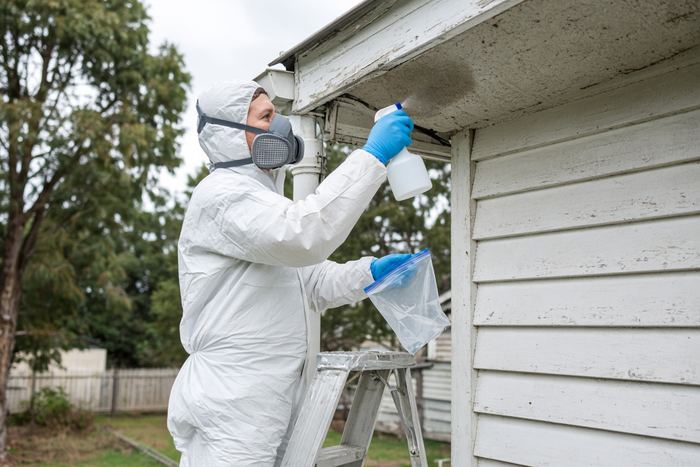Assessor in protective gear wetting an eave before taking a sample